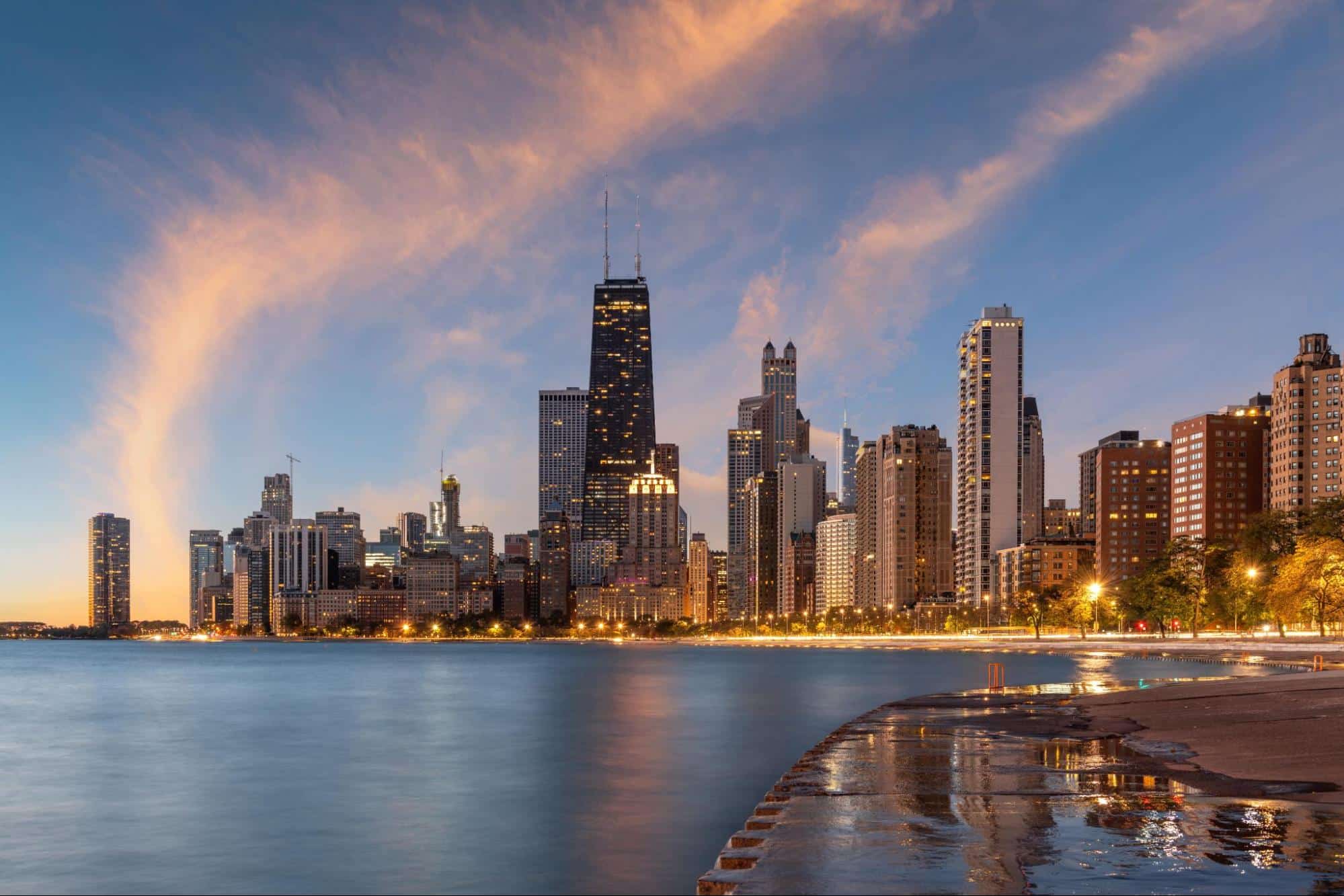 Chicago skyline at sunset viewed from the waterfront, where tall buildings reflect in calm water and wispy clouds drift aboveโa scene as meticulous and detailed as the precision found in Forensic Accounting Services.