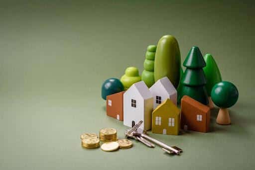 Miniature model houses and trees with a set of keys and stacks of coins in the foreground, symbolizing real estate, property investment, or home ownership—perfect for exploring what are the best REITs to invest in.